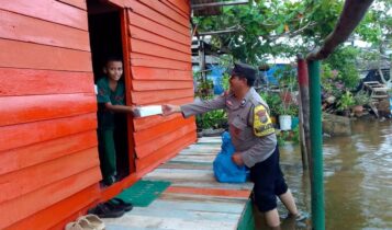 Bhabinkamtibmas kelurahan Tanjung Unggat Aiptu Rasmudi bagikan makanan kepada warga yang terdampak Banjir Rob. (Foto: Humas)