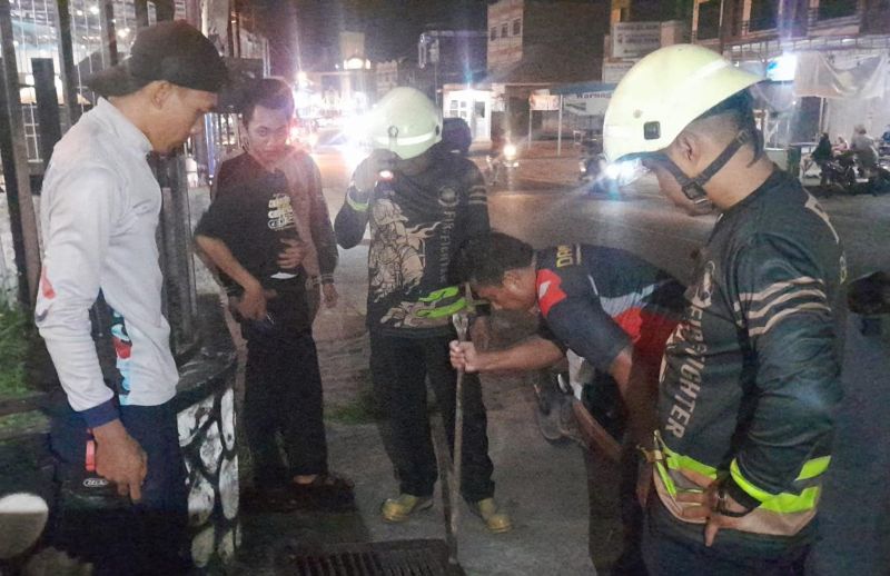Personil UPT Damkar Bintan Utara membantu mengambilkan kunci motor milik warga Tanjung Uban yang masuk ke dalam selokan dengan penjepit ular. (Foto Damkar Bintan)